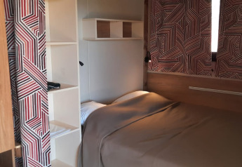 Hyggeligt glampingværelse med en dobbeltseng, åbne hylder og geometriske gardiner ved vinduet.
