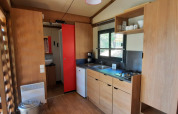 Cuisine moderne de glamping avec armoires en bois, gazinière, petit frigo et fenêtre très lumineuse.