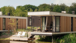 Moderne Glamping-Unterkunft mit Terrasse am Wasser, umgeben von Natur und bequemen Sonnenliegen.