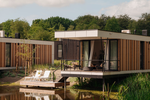 Moderne Glamping-Unterkunft mit Terrasse am Wasser, umgeben von Natur und bequemen Sonnenliegen.