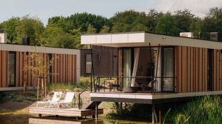Cabane de glamping moderne avec terrasse sur l'eau, entourée de verdure et transats confortables dehors.