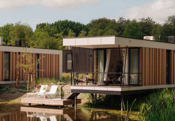 Moderne Glamping-Unterkunft mit Terrasse am Wasser, umgeben von Natur und bequemen Sonnenliegen.