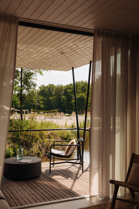 Udsigt fra et glamping-telt ud til terrasse med stol og bord, natur og strandmiljø i baggrunden.
