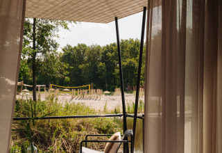 Vue depuis un hébergement glamping sur une terrasse avec fauteuil et table, paysage sableux dehors.