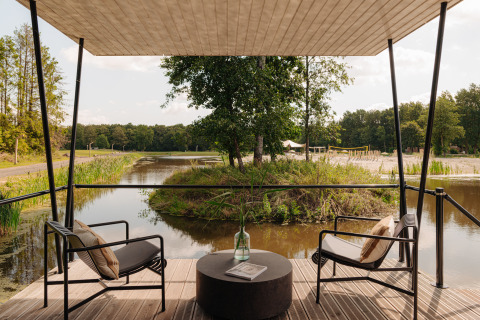 Udsigt fra terrasse med to stole ved glamping, med sø og grøn natur omkring, afslappende stemning.