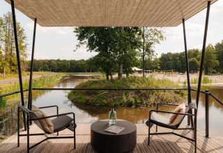 Udsigt fra terrasse med to stole ved glamping, med sø og grøn natur omkring, afslappende stemning.