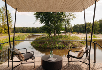 View from a glamping terrace with two chairs by the water, peaceful scenery and lush greenery around.