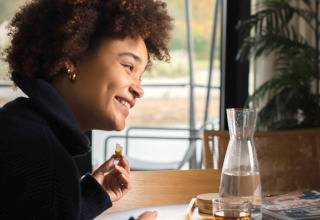 Femme souriante prenant un repas à une table dans un hébergement glamping, vue sur la nature dehors.
