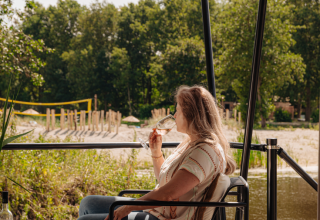 Frau entspannt mit einem Glas Wein auf der Terrasse einer Glamping-Unterkunft am Wasser.
