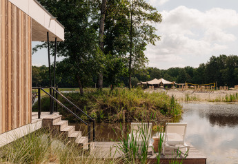 Glamping-Unterkunft am See mit Holzterrasse, Liegestühlen und Sandstrand, umgeben von Bäumen.
