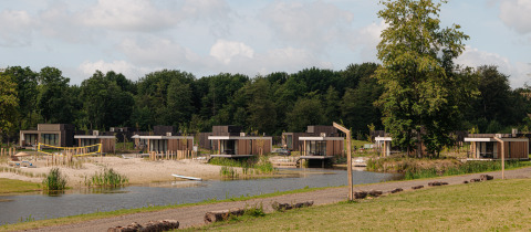 Glamping-Unterkünfte mit modernen Hütten am See, natürlicher Umgebung und Sandstrand im Vordergrund.