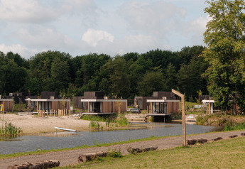 Glamping-Unterkünfte mit modernen Hütten am See, natürlicher Umgebung und Sandstrand im Vordergrund.