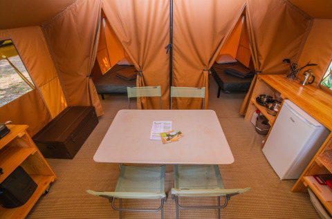 Interior of a Ponza safari tent at Onlycamp Camping Les Vailhès, with dining table, beds and kitchenette.