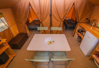 Interior de una tienda safari Ponza en Onlycamp Camping Les Vailhès, con mesa, camas y pequeña cocina.