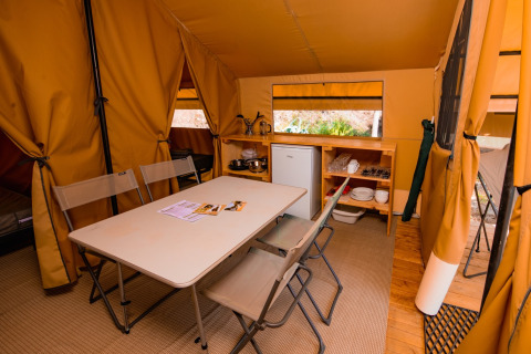 Interior of a Ponza safari tent with dining table, chairs, kitchenette, and fridge at Onlycamp Les Vailhès.