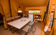 Interior de la tienda safari Ponza con mesa de comedor, sillas y cocina en Onlycamp Camping Les Vailhès.