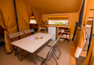 Indretning af Ponza safari-telt med spisebord, stole, tekøkken og køleskab på Onlycamp Les Vailhès.