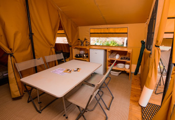 Intérieur de la tente safari Ponza avec table à manger, chaises et coin cuisine au Onlycamp Les Vailhès.