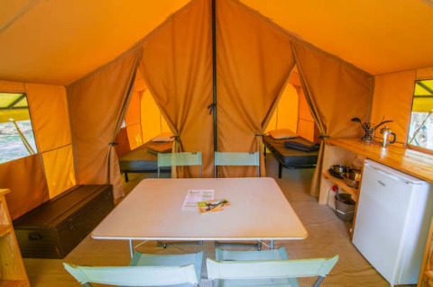 Indvendigt billede af Ponza safari-teltet på Onlycamp Camping Les Tuillères i Frankrig med spisebord og senge.
