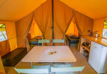 Innenaufnahme des Ponza-Safari-Zelts bei Onlycamp Camping Les Tuillères in Frankreich mit Tisch und Betten.