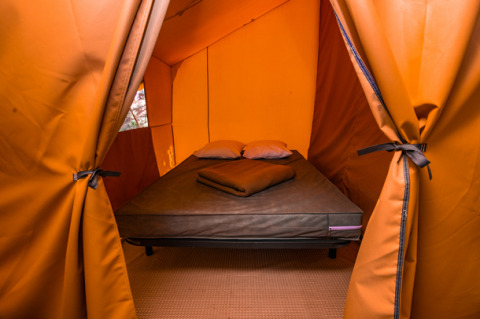 Foto af en luksuriøs glamping-teltindkvartering med en komfortabel seng, puder og tæpper indeni.