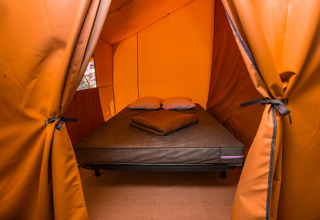 Foto van een comfortabele glamping-tentaccommodatie met bed, kussens en dekens binnenin de tent.