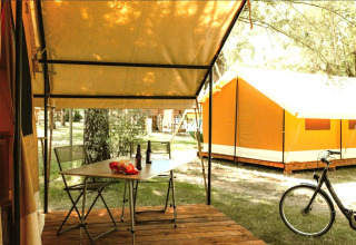 Safari-Zelt mit Terrasse, Tisch, zwei Stühlen, Getränken, Snacks und Fahrrad vor weiterem Zelt.