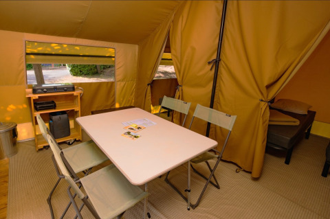 Vista interior de una tienda safari Ponza con mesa de comedor, sillas, zona de dormir y equipamiento.