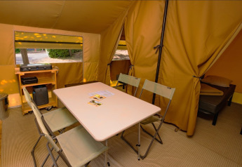 Interno della tenda safari Ponza con tavolo da pranzo, sedie, zona notte e attrezzature da campeggio.