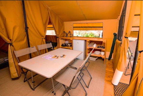 Interior of a glamping tent featuring a dining table, folding chairs, fridge, and kitchenette area.