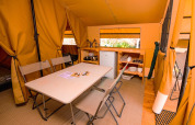 Indvendigt billede af et glamping-telt med spisebord, stole, køleskab og køkkenfaciliteter.