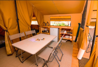 Indvendigt billede af et glamping-telt med spisebord, stole, køleskab og køkkenfaciliteter.