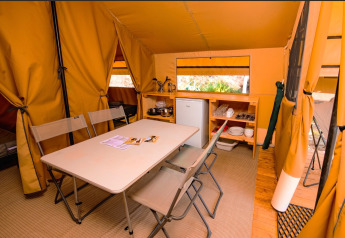 Interno di una tenda glamping con tavolo da pranzo, sedie pieghevoli, frigorifero e angolo cucina.