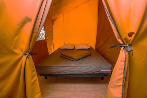 Interior view of a safari tent featuring a comfortable bed with pillows and blankets for cozy camping.