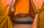 Innenaufnahme eines Safarizeltes mit einem gemütlichen Bett, Kissen und Decken für luxuriöses Camping.