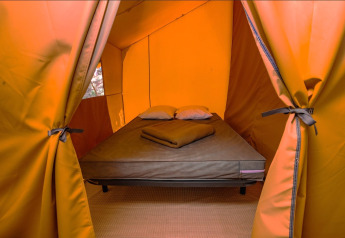 Interieur van een safaritent met een comfortabel bed, kussens en dekens voor een gezellige overnachting.