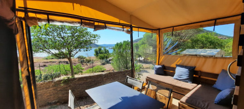 Vista desde el interior de una tienda safari con mesa y asientos hacia la naturaleza y un lago en Francia.