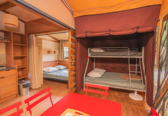 Vista interior de la tienda safari Tiny House Galli en Onlycamp Camping Les Vailhès, Francia, con literas, cama doble y cocina.