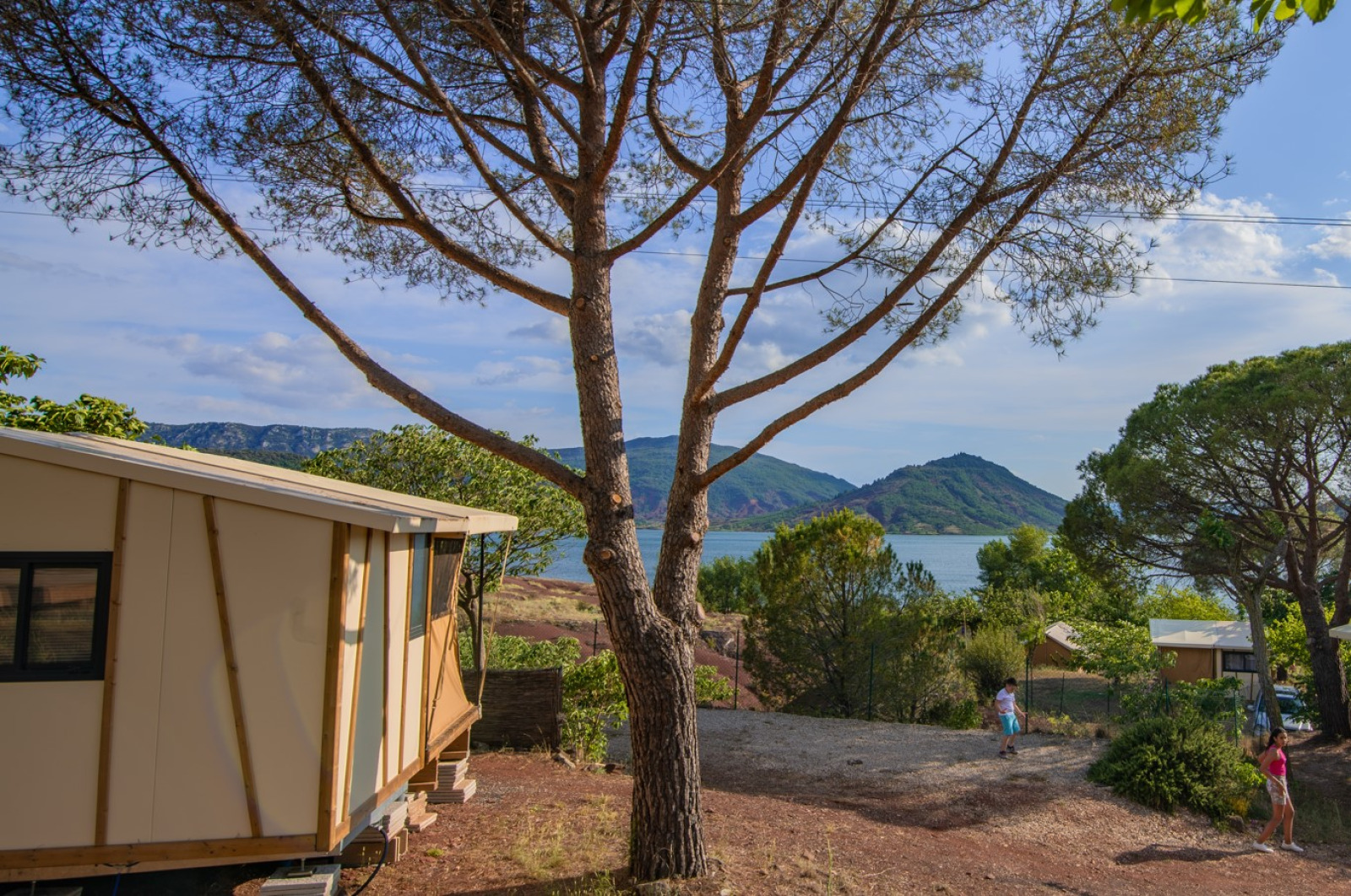 Uitzicht vanuit Tiny House Galli safaritent met bomen, meer, bergen en spelende kinderen buiten.