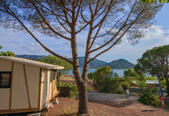 Udsigt fra Tiny House Galli safari-telt med træer, børn, sø og bjerge i baggrunden under blå himmel.