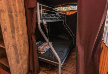 Innenansicht eines Safari-Zeltes mit Etagenbett, Holzboden und seitlich geöffneten braunen Vorhängen.