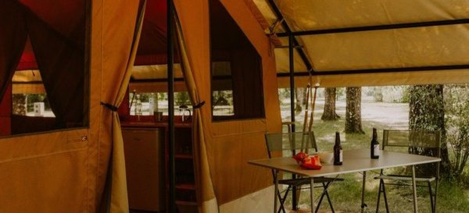 Safaritent Ponza bij Onlycamp Camping le Champ d'Eté in Frankrijk met tafel, stoelen en flessen buiten.