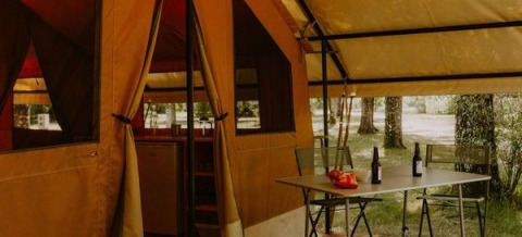 Tenda safari Ponza presso Onlycamp Camping le Champ d’Eté in Francia con tavolo, sedie e bottiglie fuori.