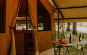 Safaritent Ponza bij Onlycamp Camping le Champ d’Eté in Frankrijk met tafel, stoelen en flessen buiten.