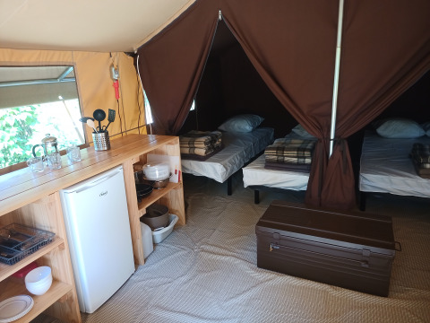 Vista interior de una tienda safari Ponza con tres camas, pequeña cocina y nevera en Camping le Champ d’Eté.