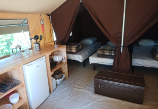 Indvendigt billede af Ponza safari-telt med tre senge, køkkenbord og køleskab på Camping le Champ d'Eté.