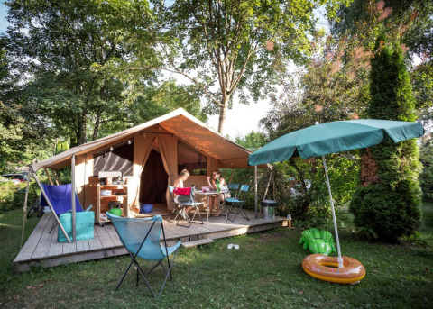 Familia descansando en tienda safari en Onlycamp Camping La Gâtine, Francia, rodeada de naturaleza verde.