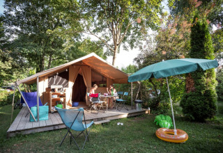 Familie slapper af foran en safari telt ved Onlycamp Camping La Gâtine i Frankrig, omgivet af grønt.