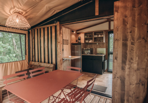 Interior de tienda safari con mesa de comedor, cocina pequeña y detalles rústicos de madera y naturaleza.