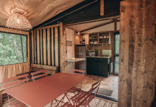 Interior de tienda safari con mesa de comedor, cocina pequeña y detalles rústicos de madera y naturaleza.